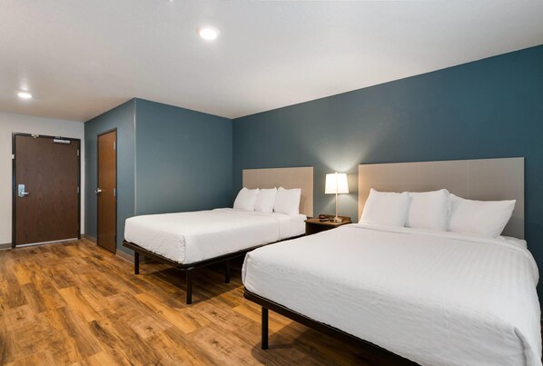 Habitación de hotel con dos camas, suelo de madera y una pared azul.