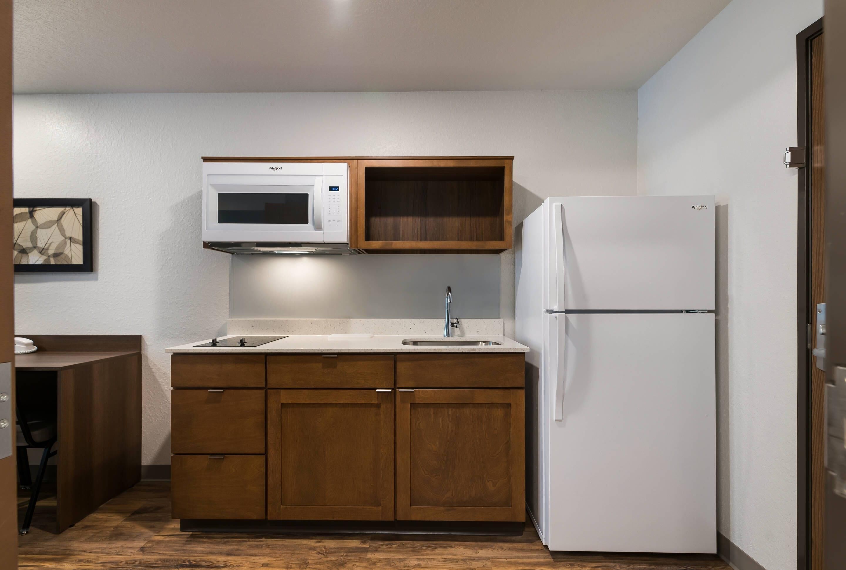 A compact kitchen with a microwave, a refrigerator, and wooden cabinets.