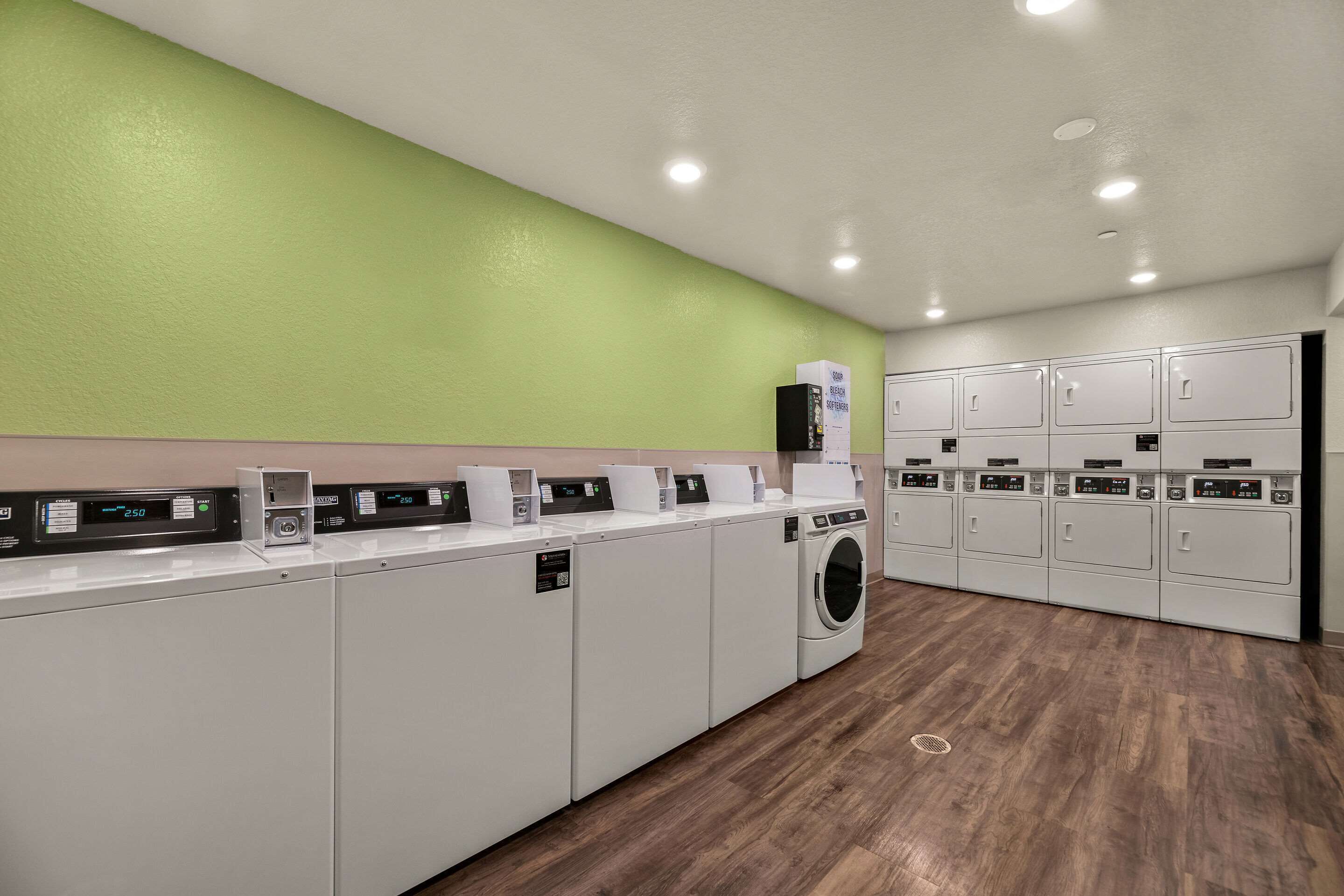Un cuarto de lavandería con varias lavadoras y secadoras, una pared verde y piso de madera.