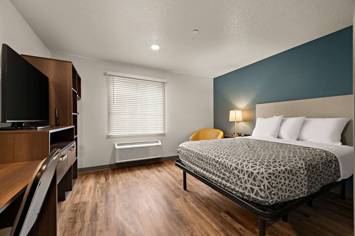 Een hotelkamer met een bed, een bureau, een televisie en een raam met jaloezieën.
