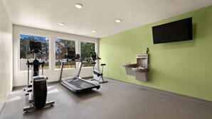 Une salle de sport équipée de tapis de course, de vélos elliptiques et d’un téléviseur fixé au mur.