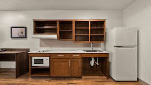Une cuisine de taille réduite, dotée de meubles en bois, d’un four à micro-ondes, d’un évier et d’un réfrigérateur.