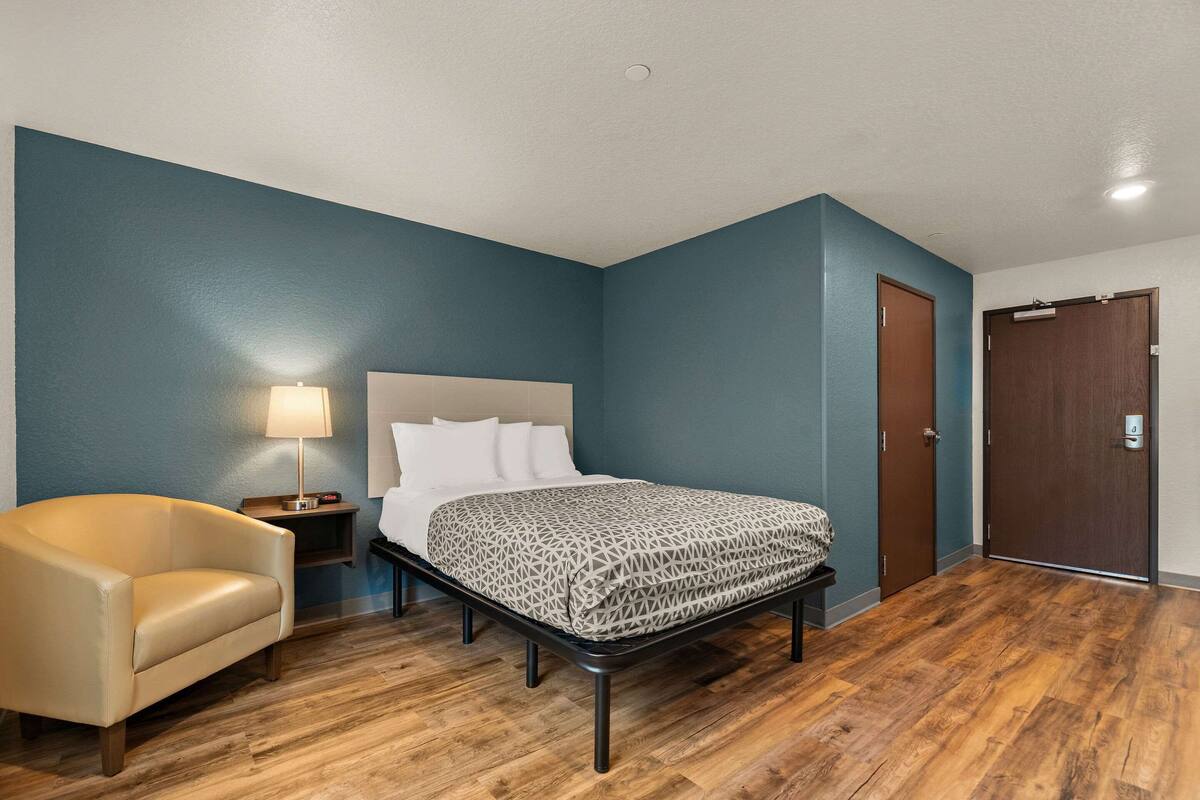 Een slaapkamer met een bed, een stoel, een nachtkastje en een deur.