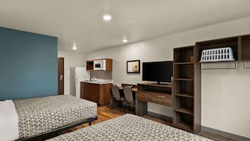 Habitación de hotel con dos camas, kitchenette, escritorio con silla, televisor y armario.
