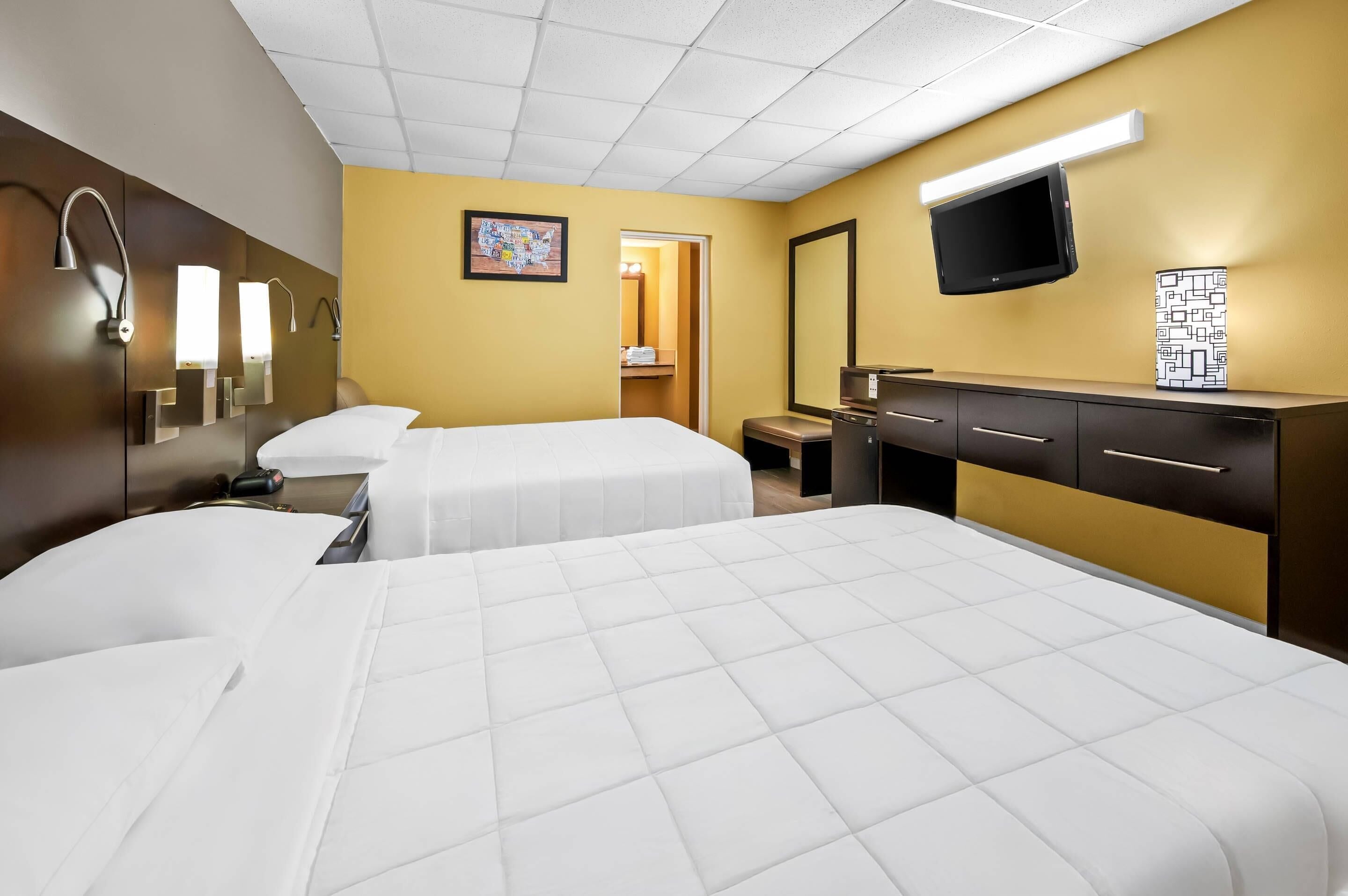 A hotel room with two beds, a desk, a TV, and a bathroom visible through an open door.