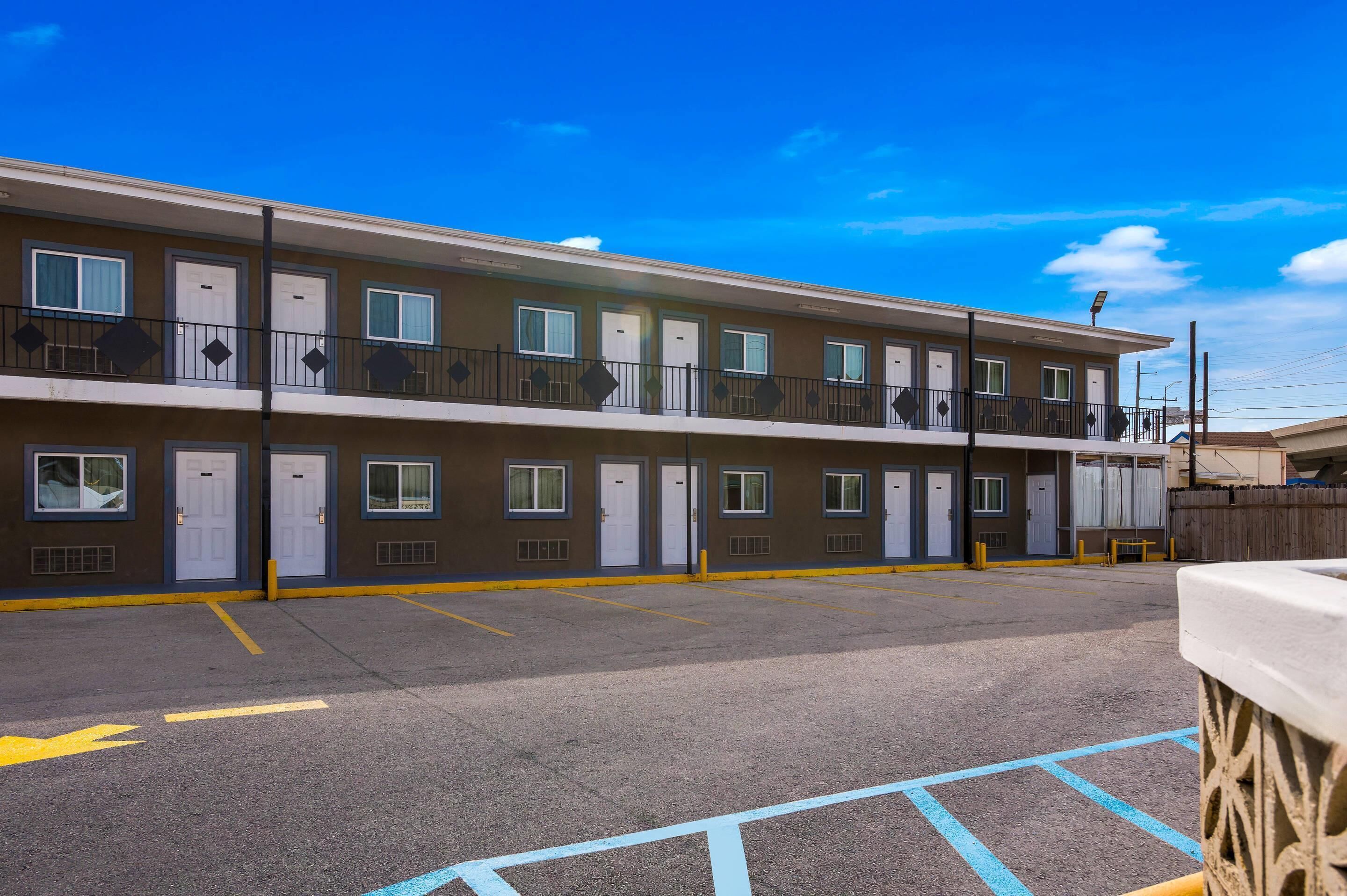 Un motel de dos pisos con una fila de habitaciones, cada una con puerta y ventana, y un balcón.