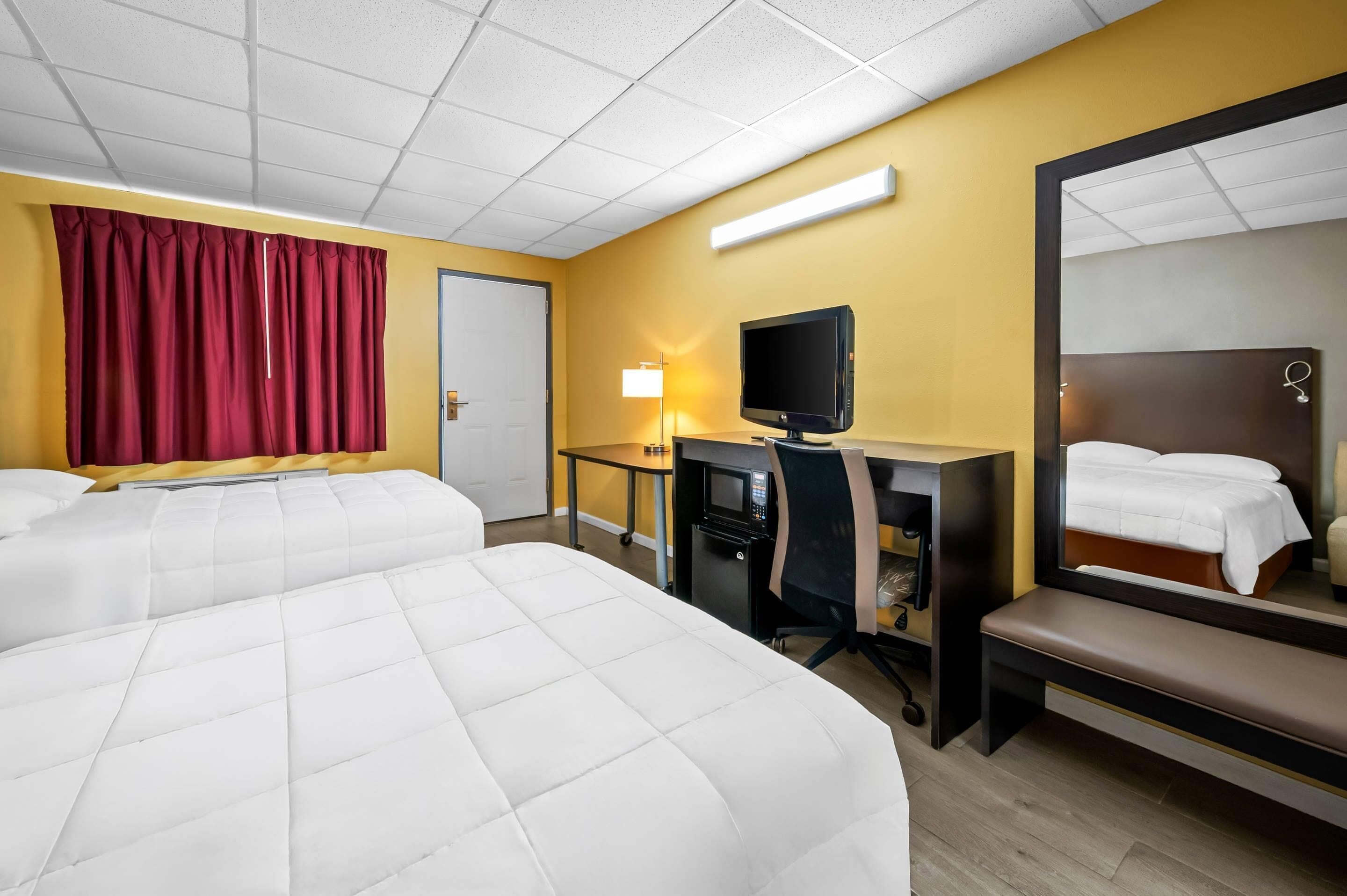 A hotel room with two beds, a desk with a TV, a mirror, and a bedside table.