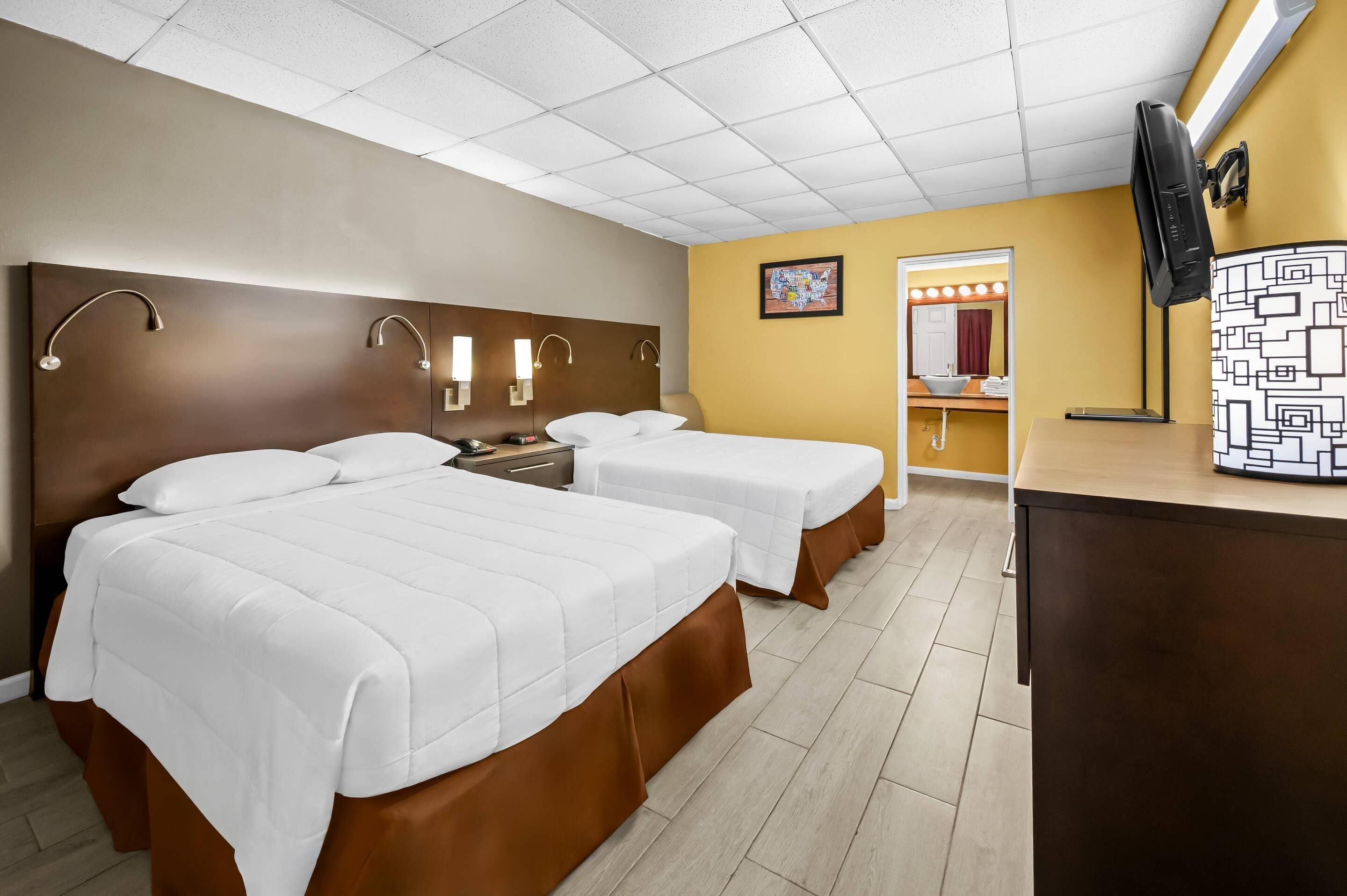 Een hotelkamer met twee bedden, een bureau, een televisie en een badkamer die door een open deur zichtbaar is.