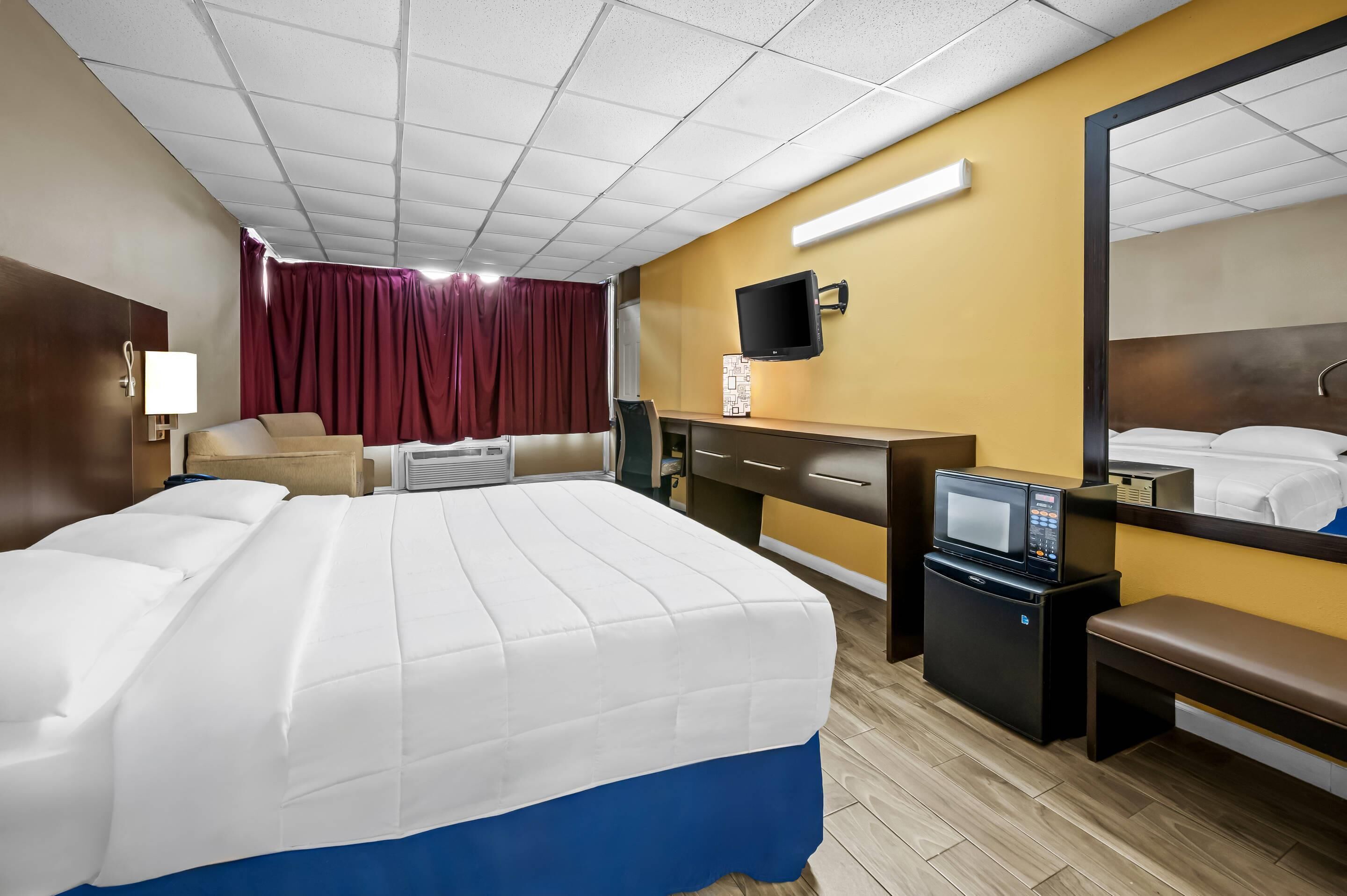 A hotel room with a bed, desk, chair, TV, microwave, and a mirror.