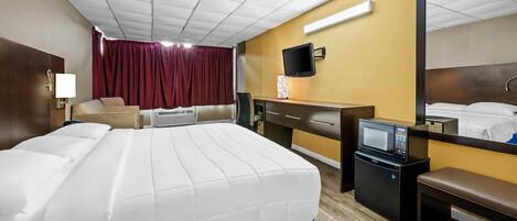 A hotel room with a bed, desk, chair, TV, microwave, and a mirror.
