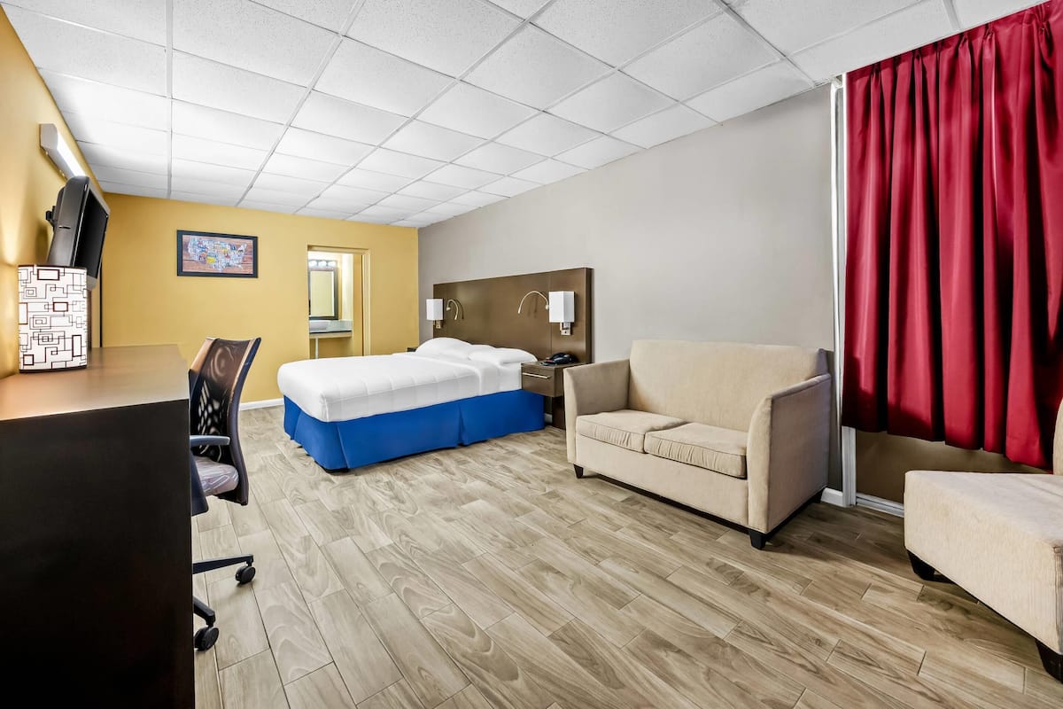 Quarto de hotel com cama, escrivaninha, cadeira, sofá e cortina vermelha.