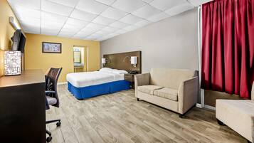 Een hotelkamer met een bed, een bureau, een stoel, een bank en een rood gordijn.