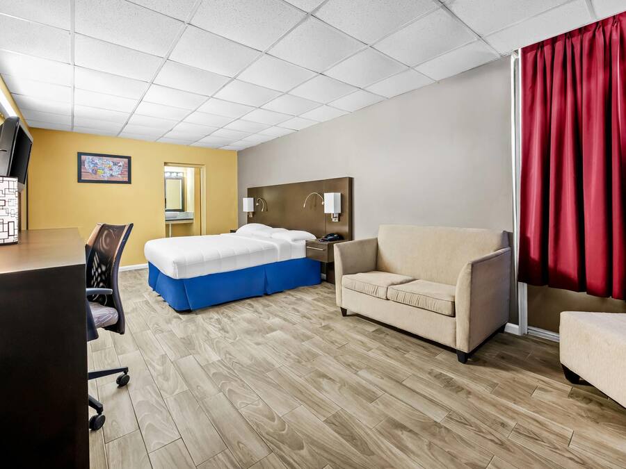 Een hotelkamer met een bed, een bureau, een stoel, een bank en een rood gordijn.