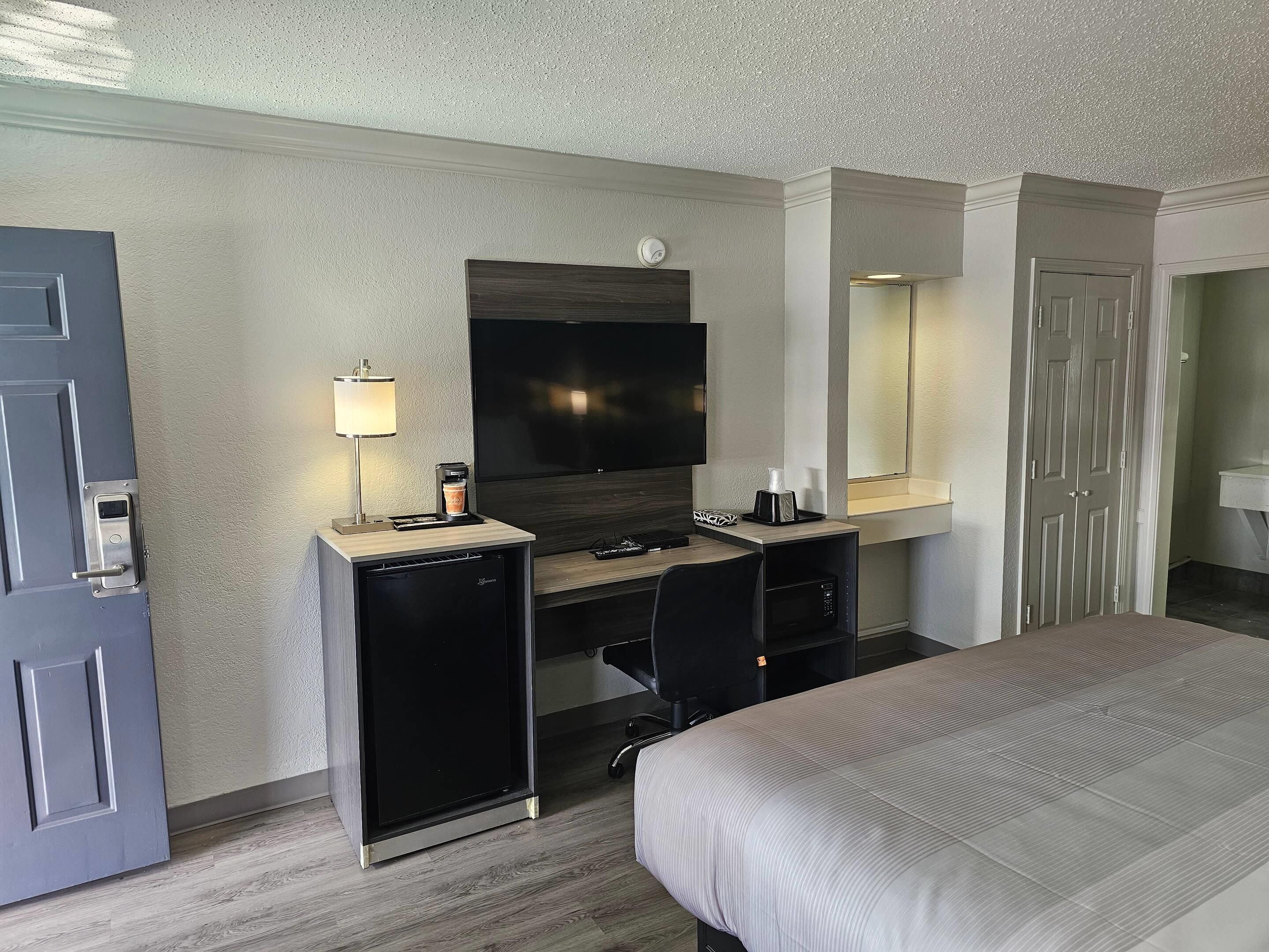 Una habitación de hotel con cama, escritorio, computadora, televisor, cafetera y minibar.
