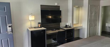 Una habitación de hotel con cama, escritorio, computadora, televisor, cafetera y minibar.