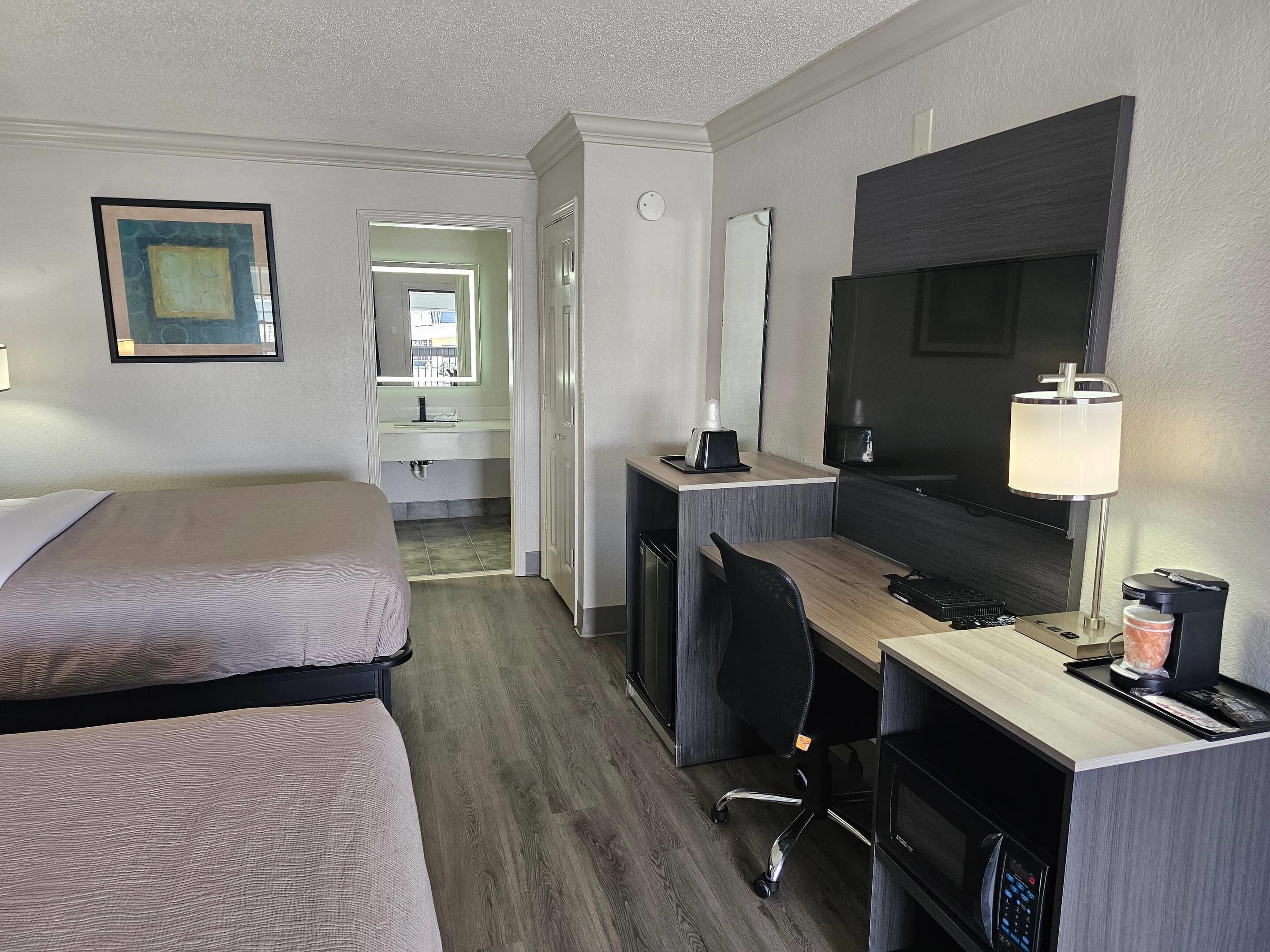 A hotel room with a bed, desk, chair, TV, and a bathroom visible in the background.