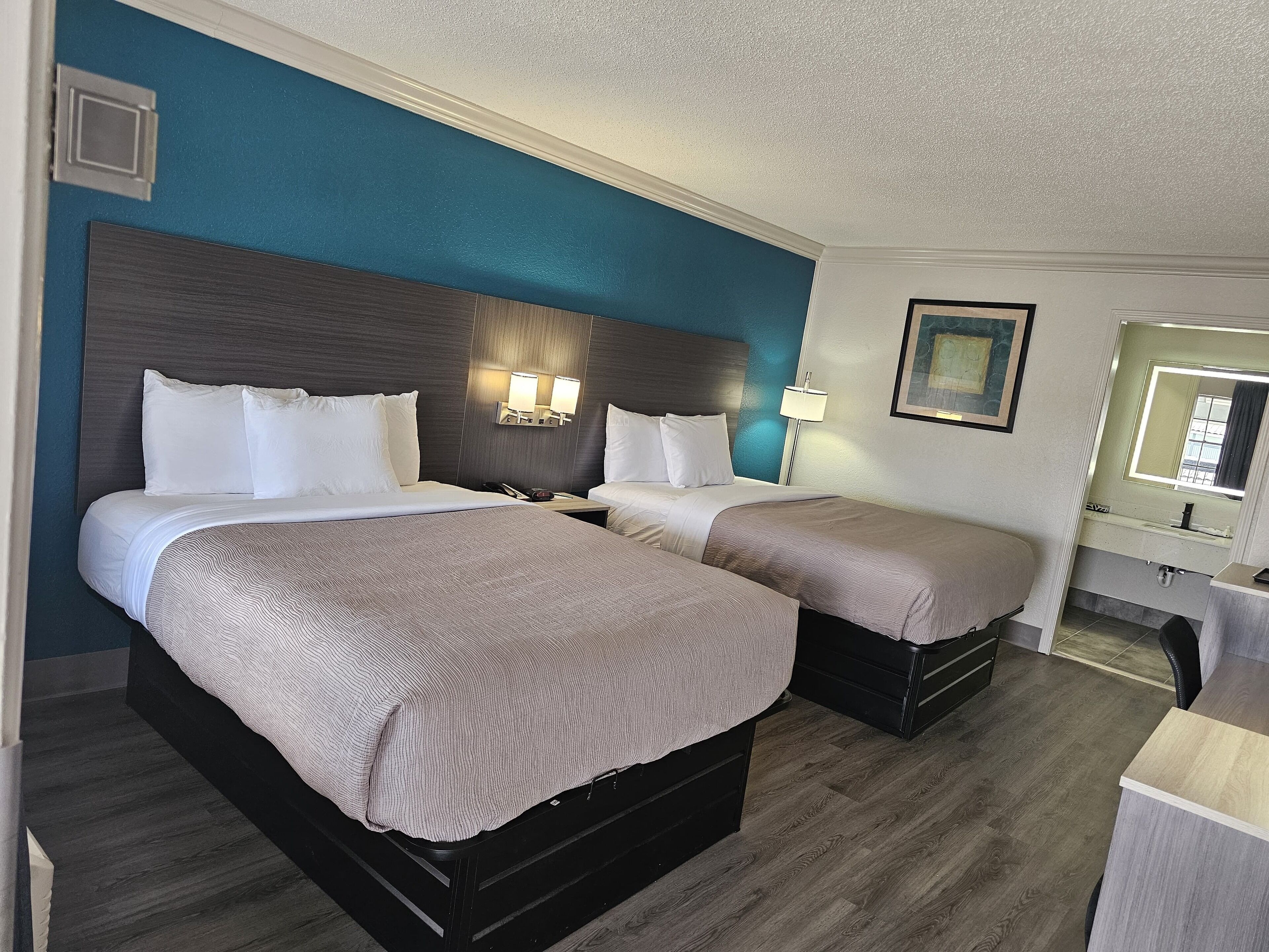 A hotel room with two beds, a nightstand, a lamp, and a mirror.