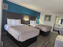 A hotel room with two beds, a nightstand, a lamp, and a mirror.