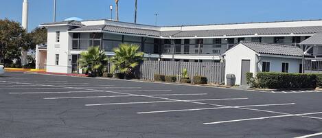 Un motel con estacionamiento, área cercada y palmeras.