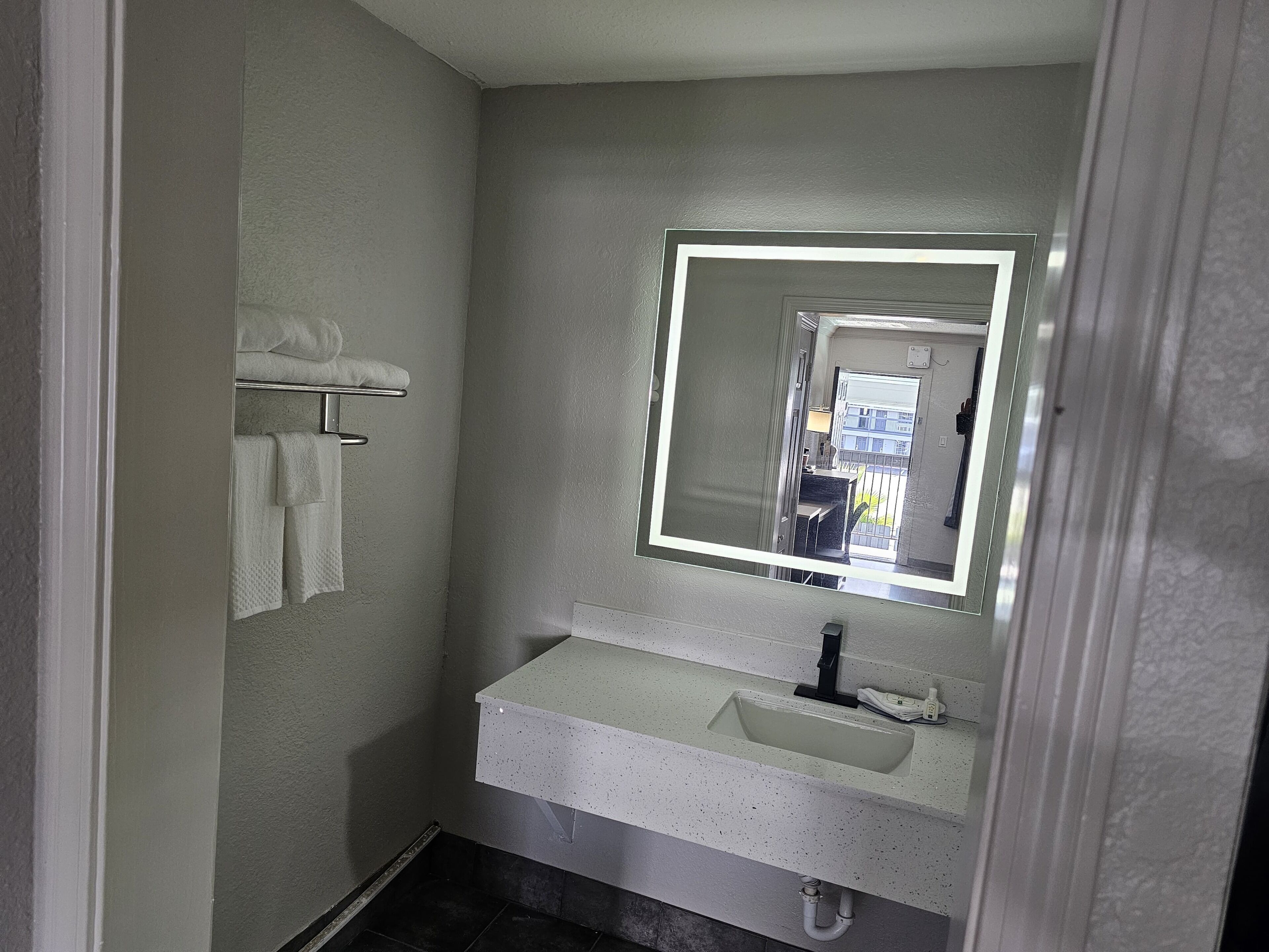 Un baño con lavamanos blanco, espejo y toallero.