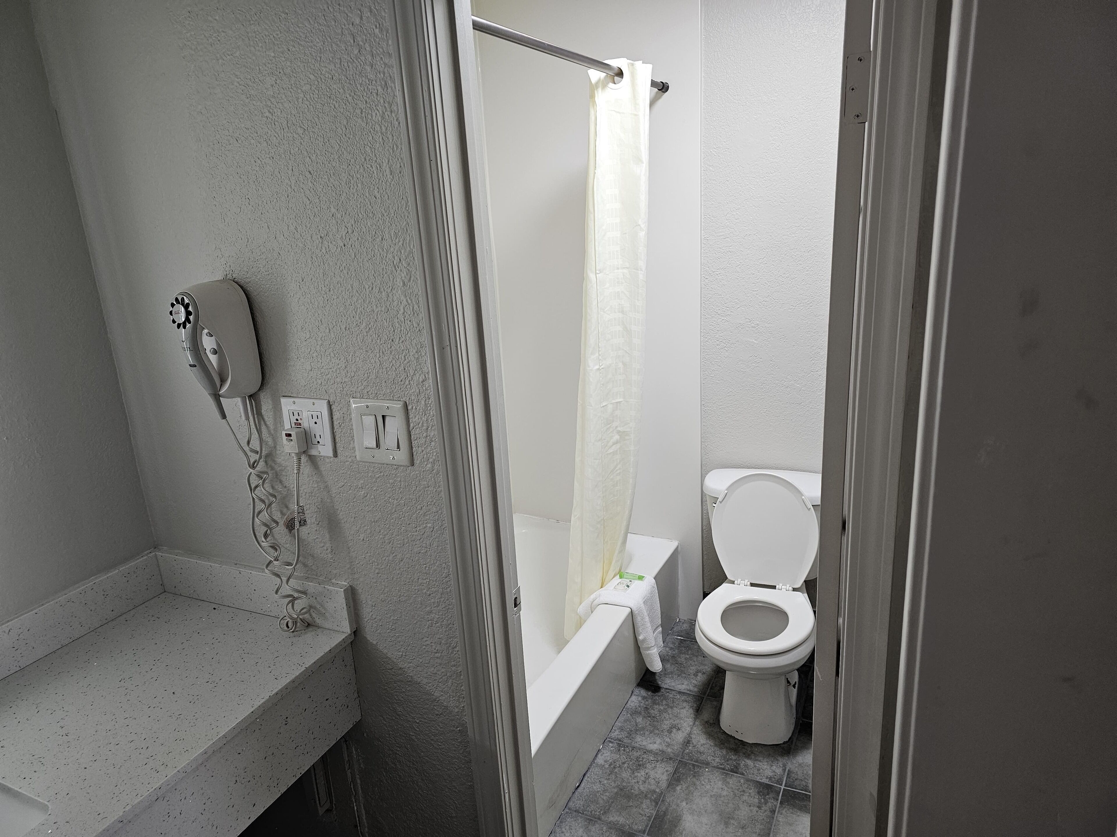 A bathroom with a shower, toilet, and a hairdryer on the wall.