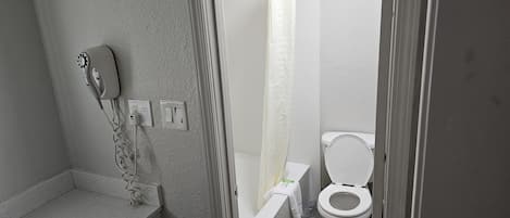 Une salle de bain équipée d’une douche, de toilettes et d’un sèche-cheveux fixé au mur.
