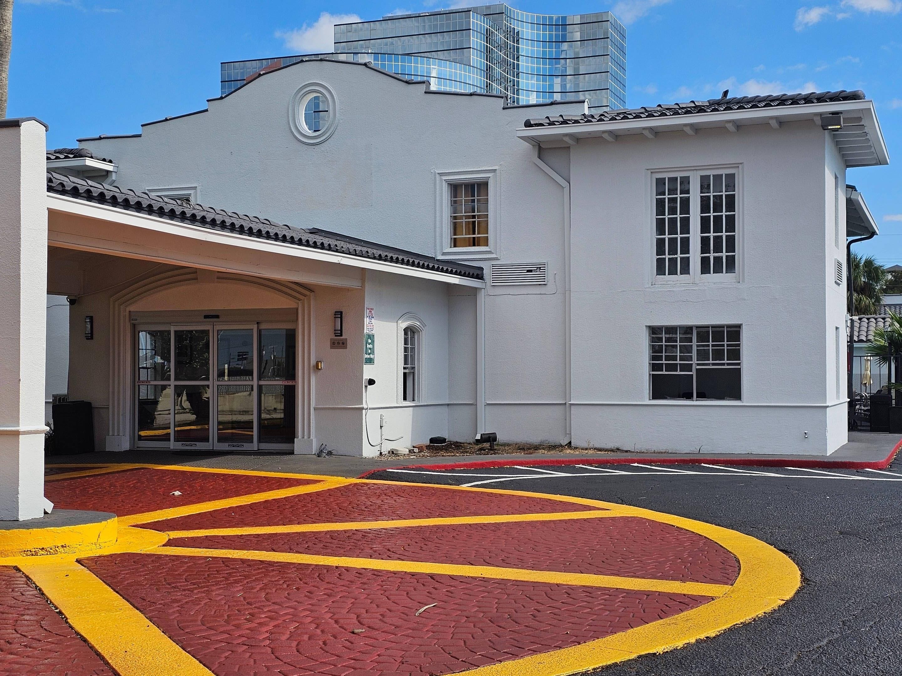 A building with a white facade, a tiled roof, and a red and yellow parking area.