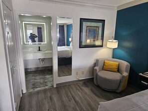 A hotel room with a bathroom, a bed, a chair, and a painting on the wall. - Quality Inn & Suites (Metairie)
