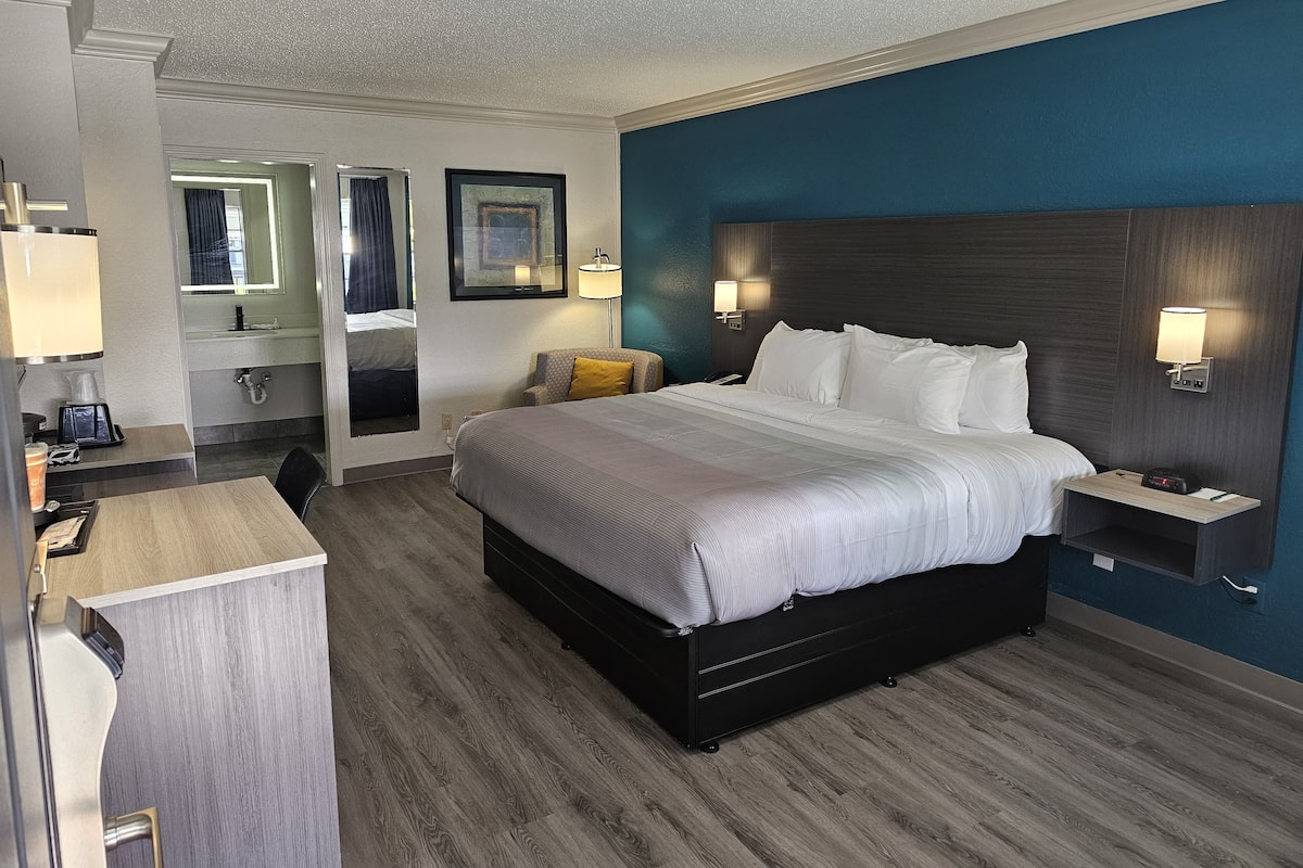 A hotel room with a large bed, bedside tables, a desk, and a mirror.