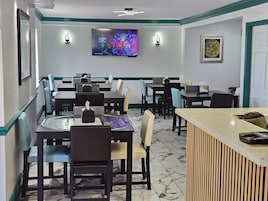 Un restaurante con mesas y sillas, un televisor en la pared y una recepción.
