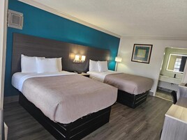 Una habitación de hotel con dos camas, una mesita de noche, una lámpara, un espejo y suelo de madera.