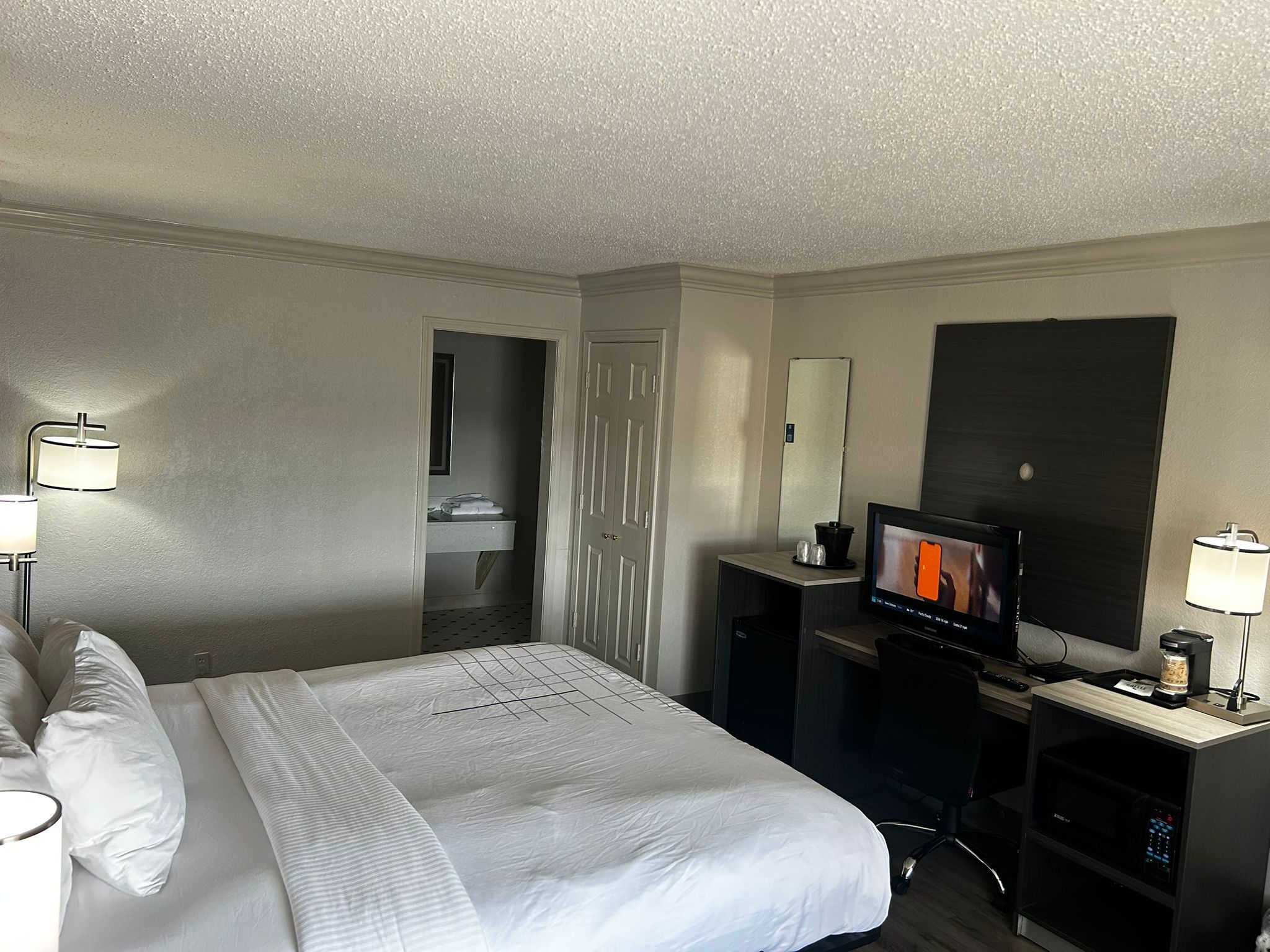 A hotel room with a bed, a desk with a television, a coffee machine, and a minibar.