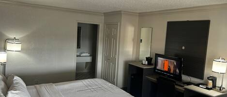 A hotel room with a bed, a desk with a television, a coffee machine, and a minibar.