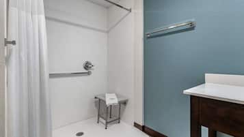 A bathroom with a shower, a small table with a towel, a handrail, and a sink.