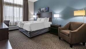 A hotel room with a bed, bedside tables, a chair, a desk, and a large window with curtains. - Sleep Inn & Suites Milwaukee/Franklin (Franklin)