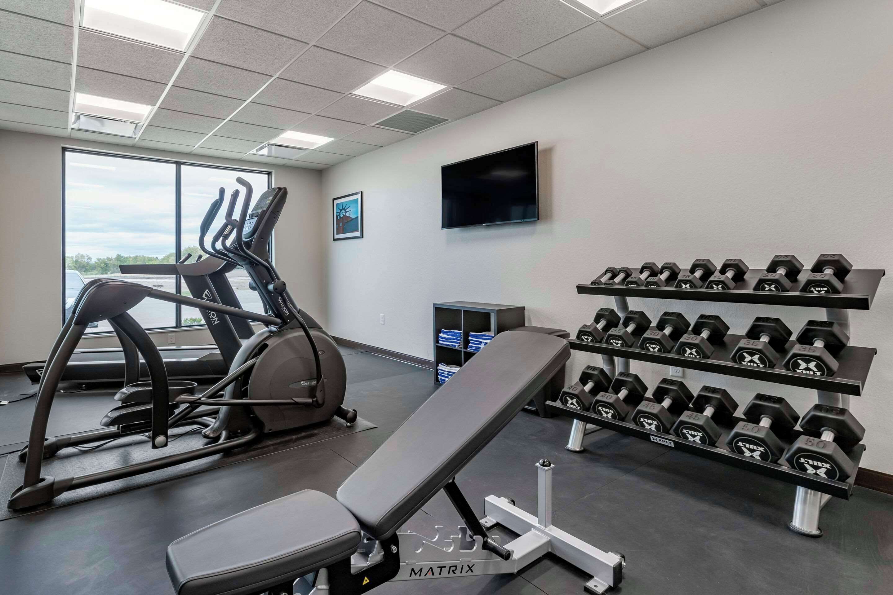 Un gimnasio con equipo de cardio, mancuernas y una banca.