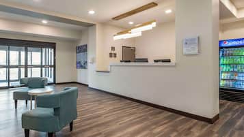 A reception area with a counter, seating, a refrigerator stocked with beverages, and a large window.