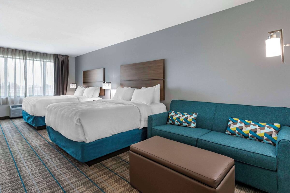 A hotel room with two beds, a sofa, a coffee table, and a large window with curtains.
