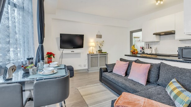A modern living room with a grey sofa, dining table, and a TV mounted on the wall.