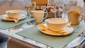 A dining table set with bowls, cups, and a pitcher, with lace curtains and a view of buildings in the background.