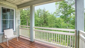 Une véranda en bois avec une balustrade blanche, un banc et une vue sur une zone boisée.