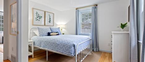 A bedroom with a bed, bedside table, lamp, and a window with curtains.