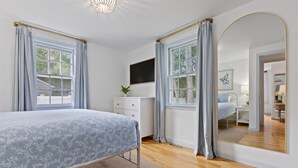 Quarto com cama, cômoda, televisão e um espelho grande.