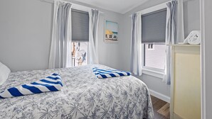 A bedroom with a bed, curtains, a painting, and a towel rack. - Steps from Hampton Beach and all entertainment! 2 bedrooms, pet friendly! (Hampton)