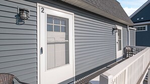 A house with a white door, a porch with a chair, and a number '2' on the door. - Steps from Hampton Beach and all entertainment! 2 bedrooms, pet friendly! (Hampton)