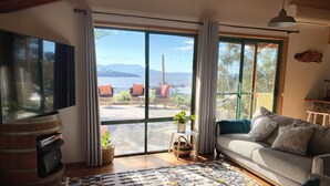 A living room with a large window, a television, a sofa, and a patterned rug. - Beautiful Orford with Maria Island Views.
Pet Friendly and Loads of Space (Orford)