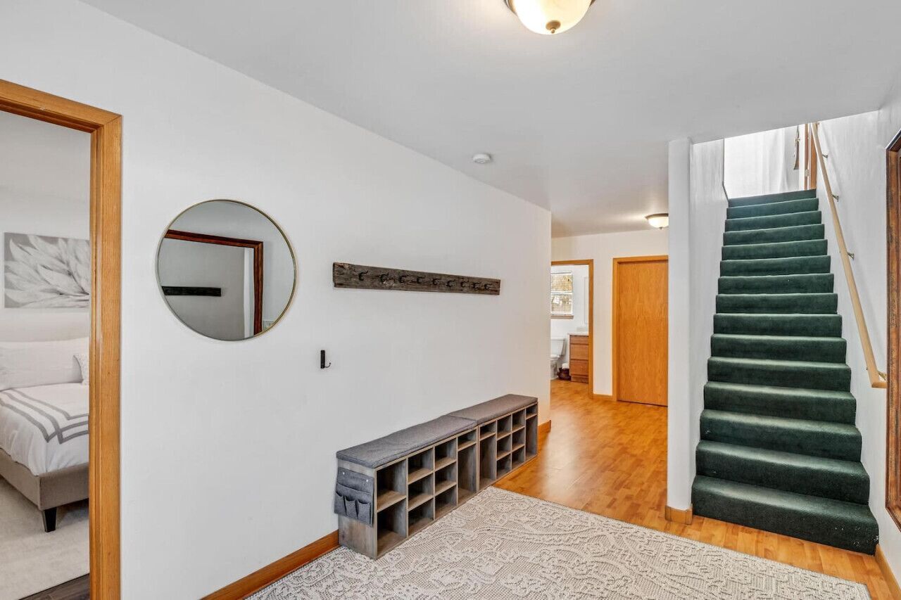 A hallway with a wooden bench, a round mirror, a wooden sign, and a green carpeted staircase.