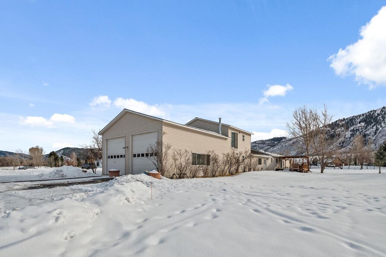 Une maison de plain-pied avec un garage, entourée de terrain enneigé et avec des montagnes en arrière-plan.