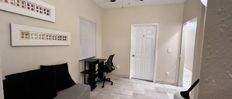 A room with a ceiling fan, a desk with a chair, a couch, and a door.