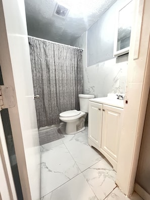 A bathroom with a toilet, a shower curtain, a sink, and a mirror.